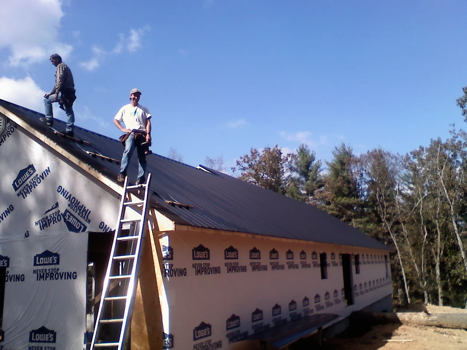 Two roofers standing on a long dark metal roof over a wrapped building in Kennewick