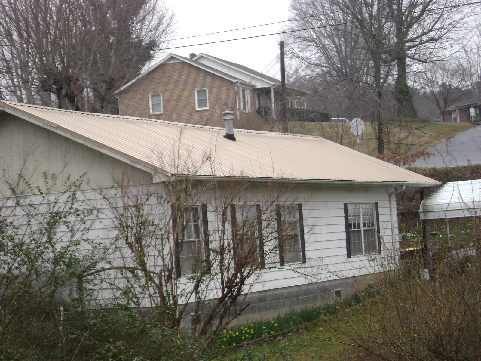 Tan metal roof on a white sided house set into a hillside — Commercial Roofing by Roofing Brothers in Kennewick